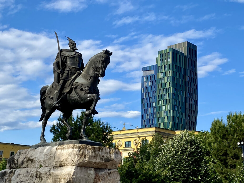 Bronze statue of Skanderbeg on horseback in Skanderbeg Square, Tirana, with a modern tower behind it