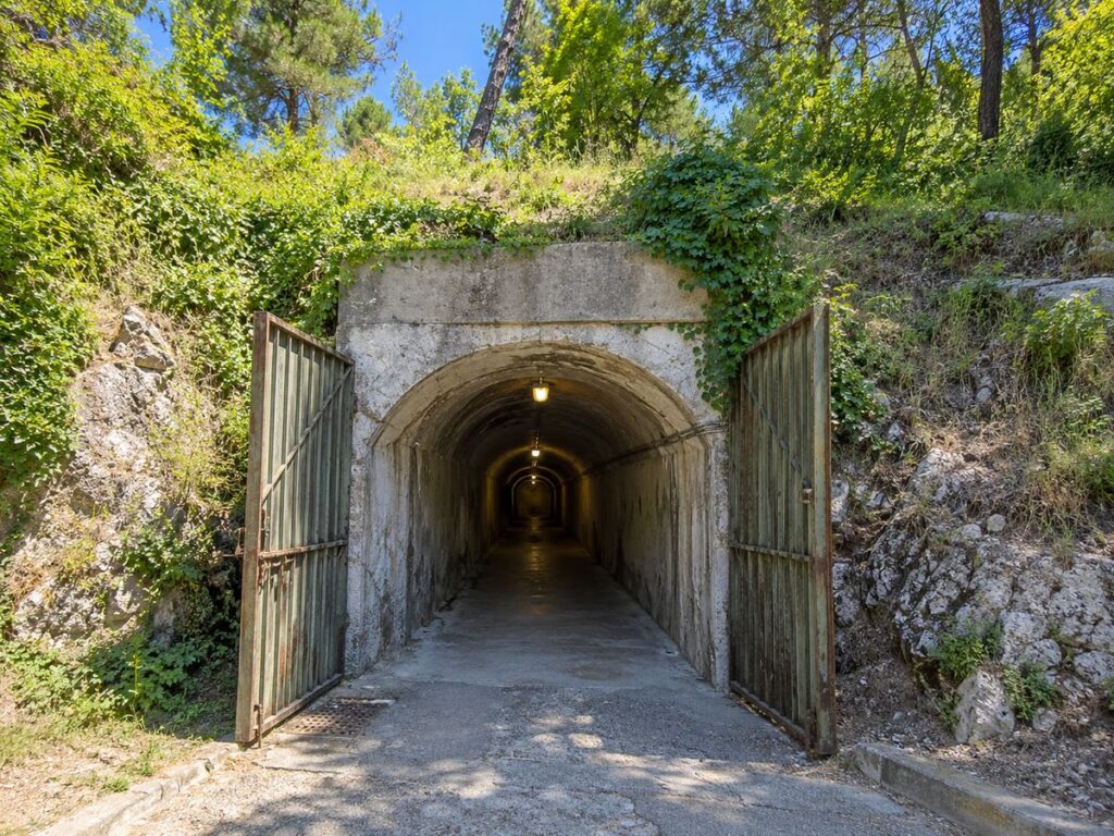 Concrete access tunnel and open metal gates at Bunk’Art 1 in a leafy hillside on Tirana’s eastern edge