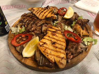Mixed grill platter with grilled chicken, meats, red peppers and lemon on a wooden board at Tymi King Pils, Tirana